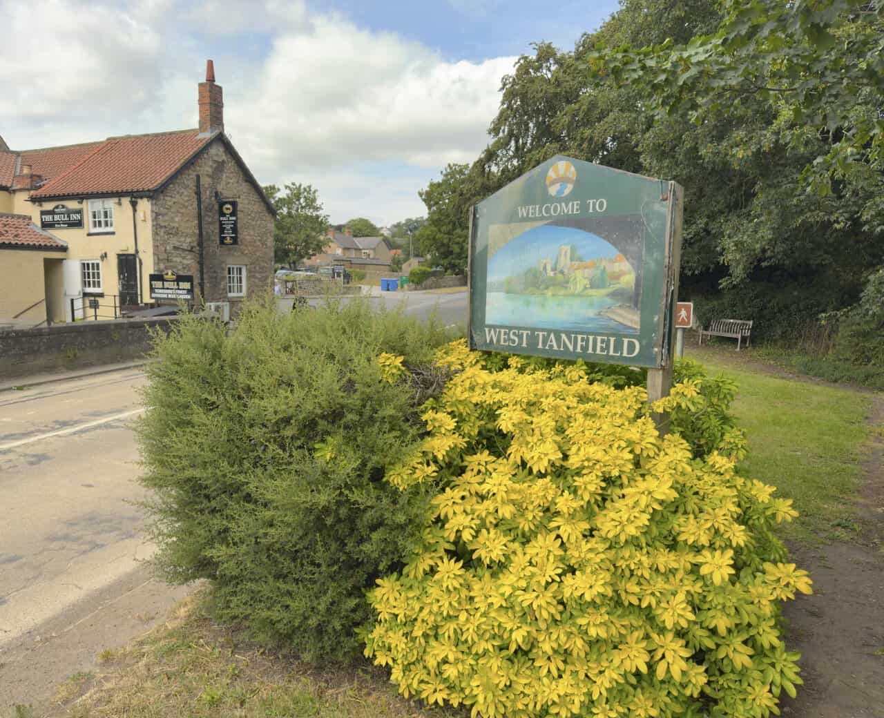 West Tanfield welcome sign surrounded by bright yellow foliage near Tanfield Bridge and the Bull Inn.