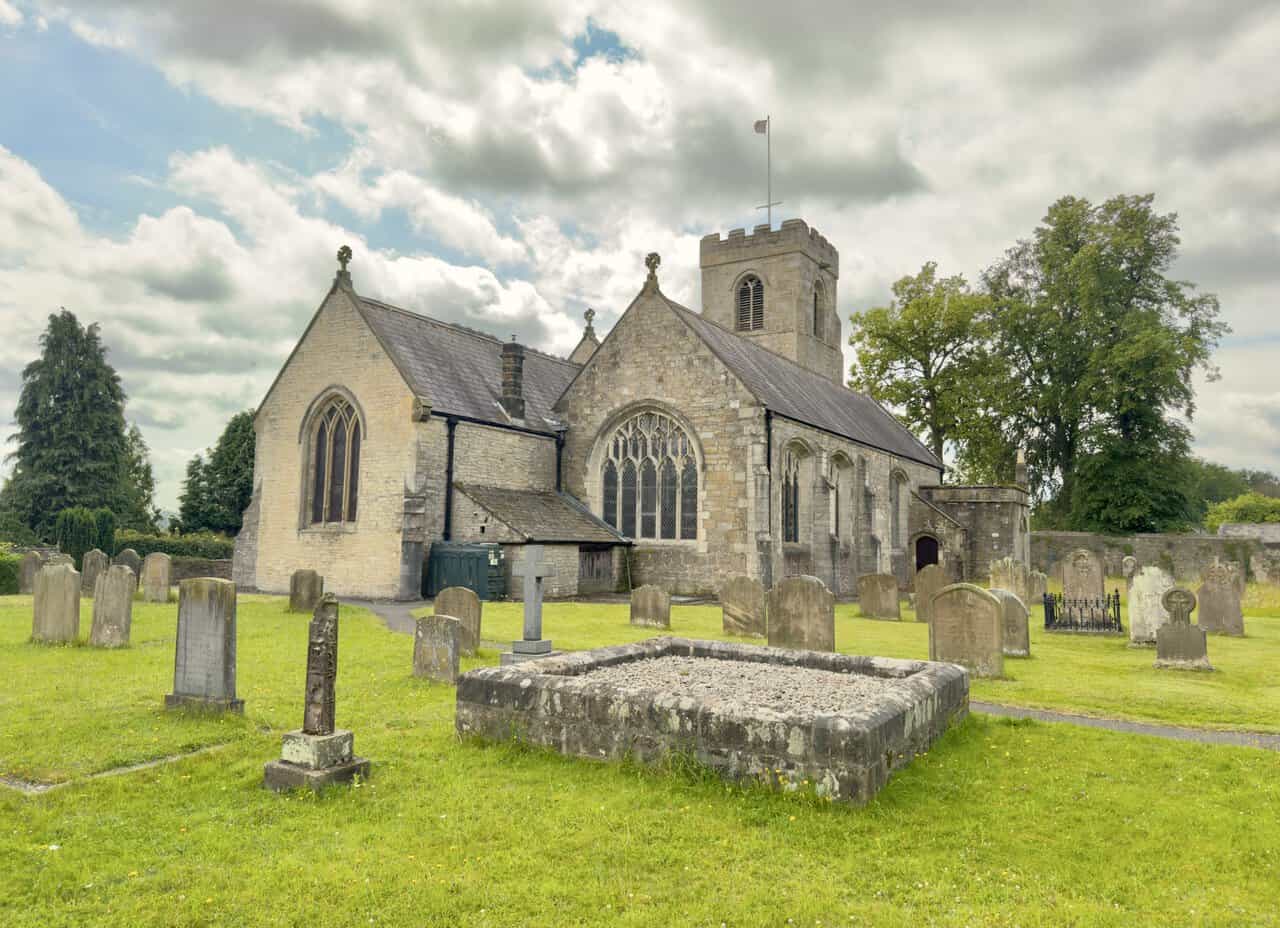 Full side view of St Nicholas’s Church showing its steep roofs, traceried windows, tower and historic churchyard.