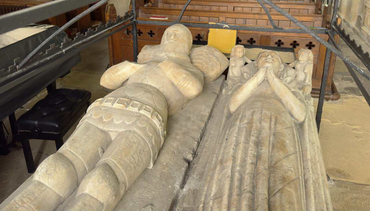 Alabaster tomb and medieval effigies of Sir John and Lady Elizabeth Marmion beneath a rare wrought-iron candle hearse.