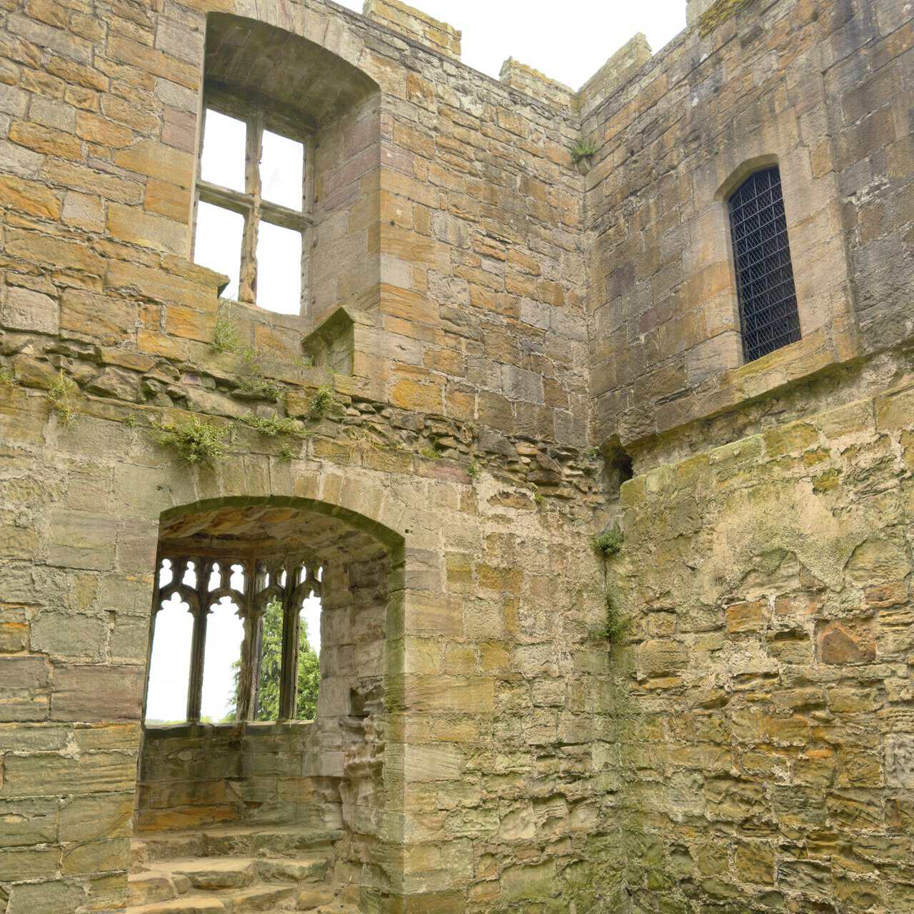 Roofless grand chamber inside Marmion Tower with bare stone walls, a fireplace and an ornate Perpendicular oriel window.