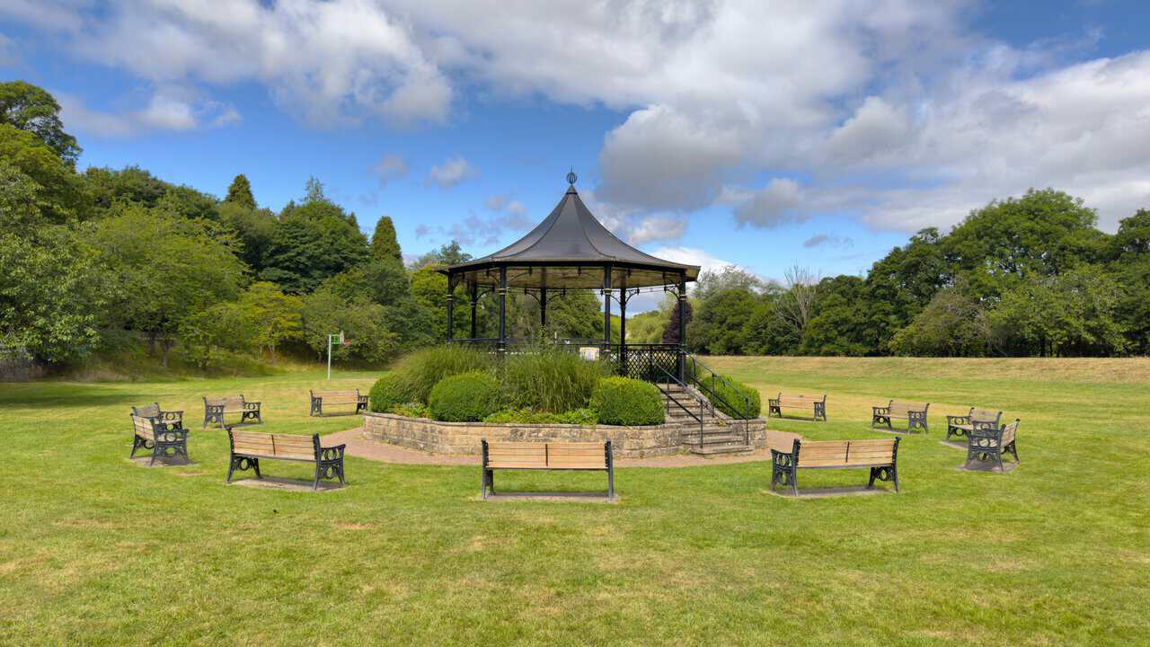 Ornate black bandstand in Bewerley Recreation Ground, surrounded by a ring of wooden benches on the grass.