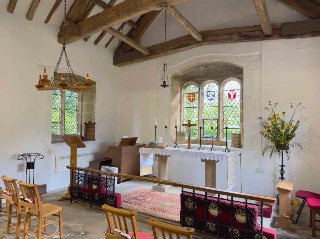 Another view inside Bewerley Grange Chapel, with leaded windows, a stone floor and wooden chairs.