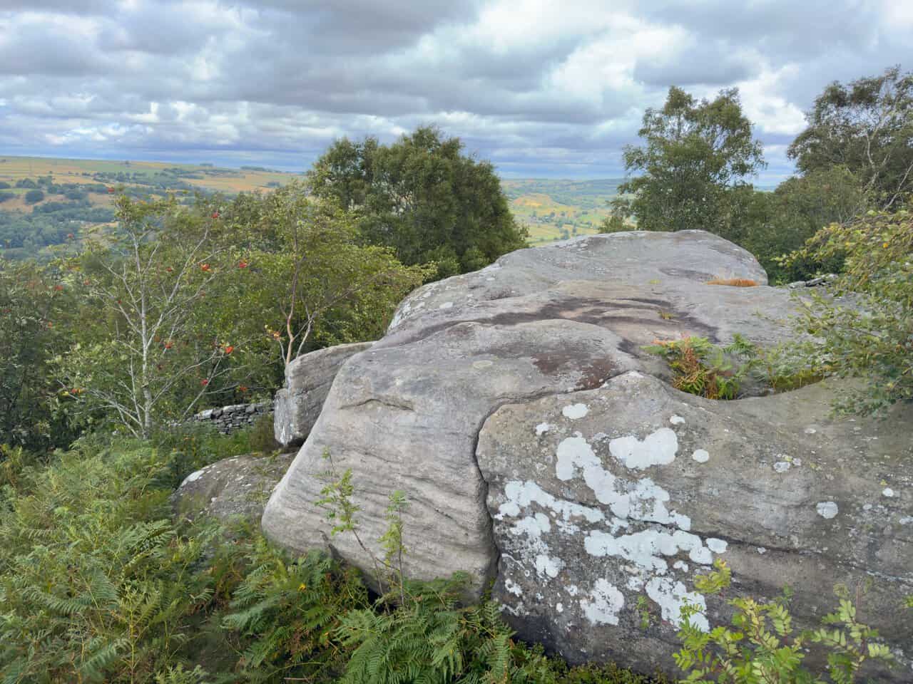 More lichen-covered gritstone outcrops on the moor, with the Nidderdale valley visible beyond.