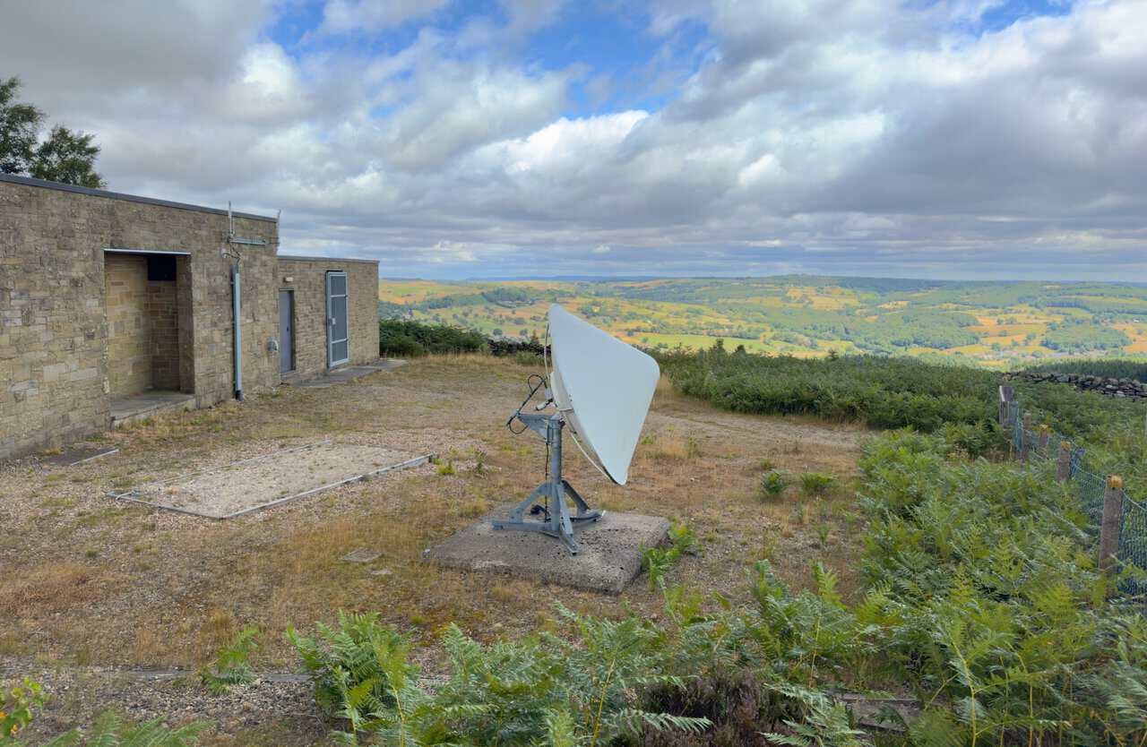 The stone building at the base of the telecommunications mast on the Yorke's Folly walk, with a satellite dish and views over Nidderdale.