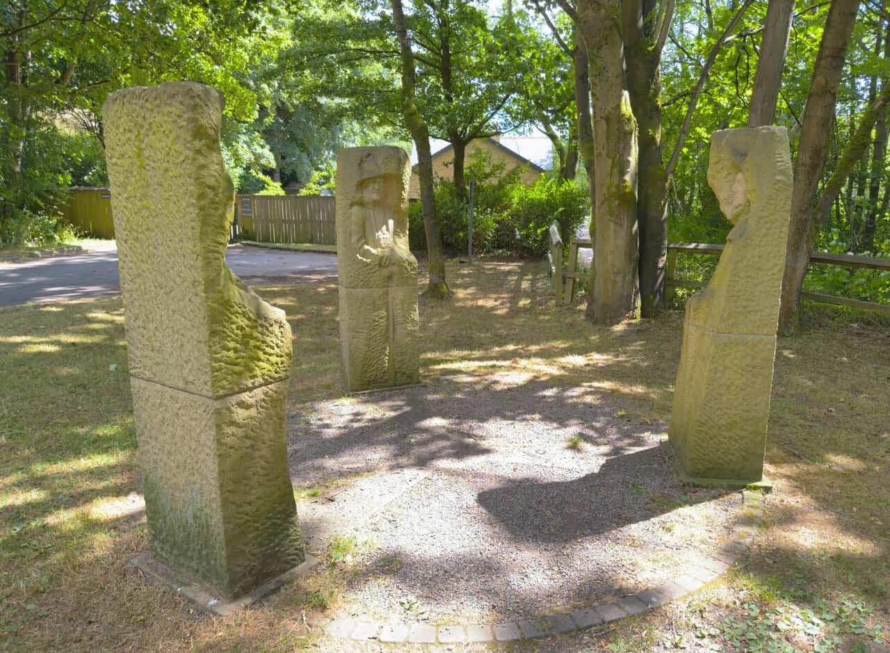 The Pillars Past sculpture near Pateley Bridge, three carved sandstone figures arranged in a circle among trees.