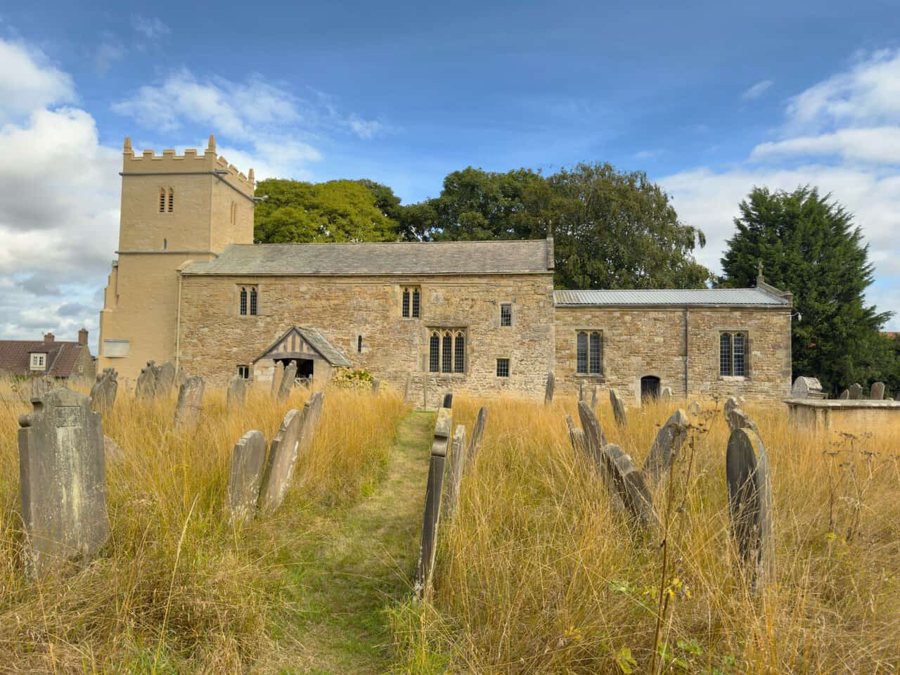 Mown path through the churchyard leading to the timber-framed porch of St Martin's Church.