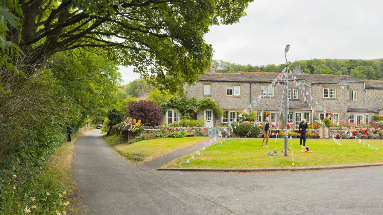 Stone cottages and a well-kept green at Langcliffe Garth, decorated with bunting and scarecrows.