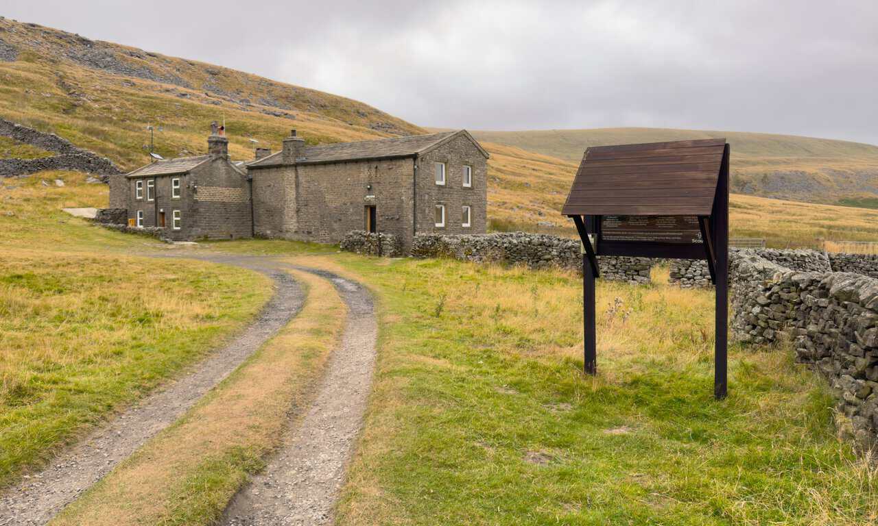 The stone hostel buildings at Hag Dyke, with a Scout information board standing beside the track.