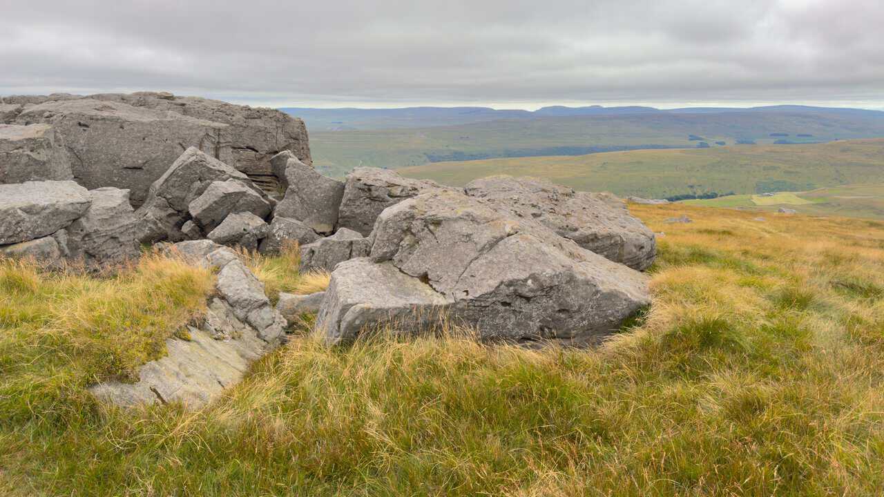 Boulders on the mountain top, with the Yorkshire Three Peaks in silhouette on the western horizon.