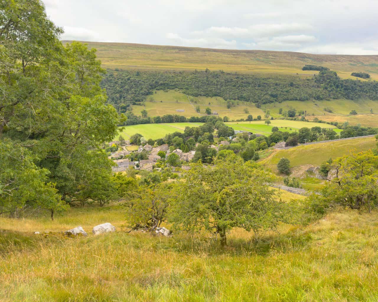 The rooftops of Starbotton seen through trees, with Moor End Fell rising behind the village. A highlight on this Great Whernside circular walk.