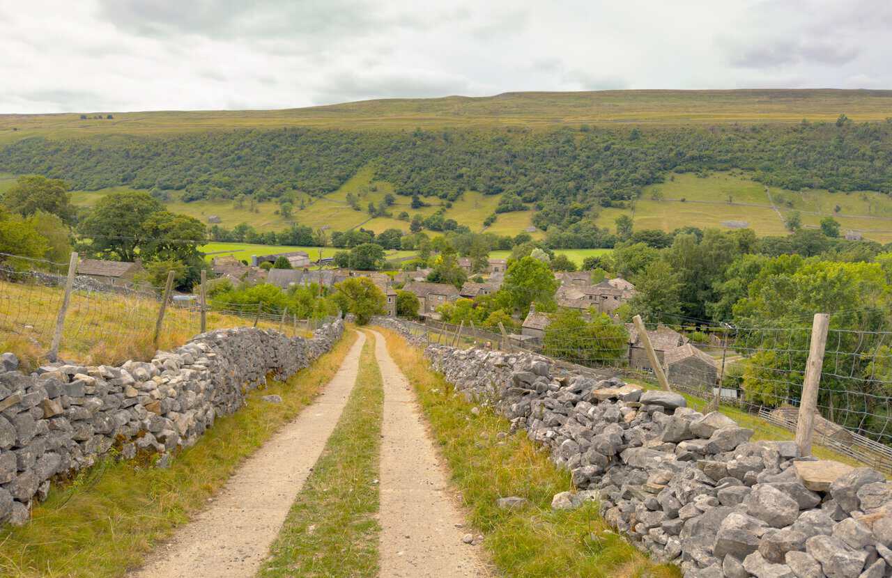 The walled stony track of Starbotton Cam Road descending towards the rooftops of Starbotton.
