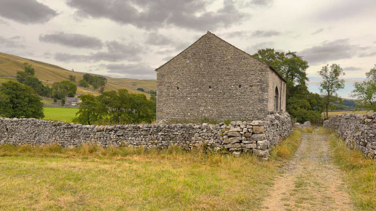 A stone field barn beside the walled track, with Kettlewell village school visible in the distance.