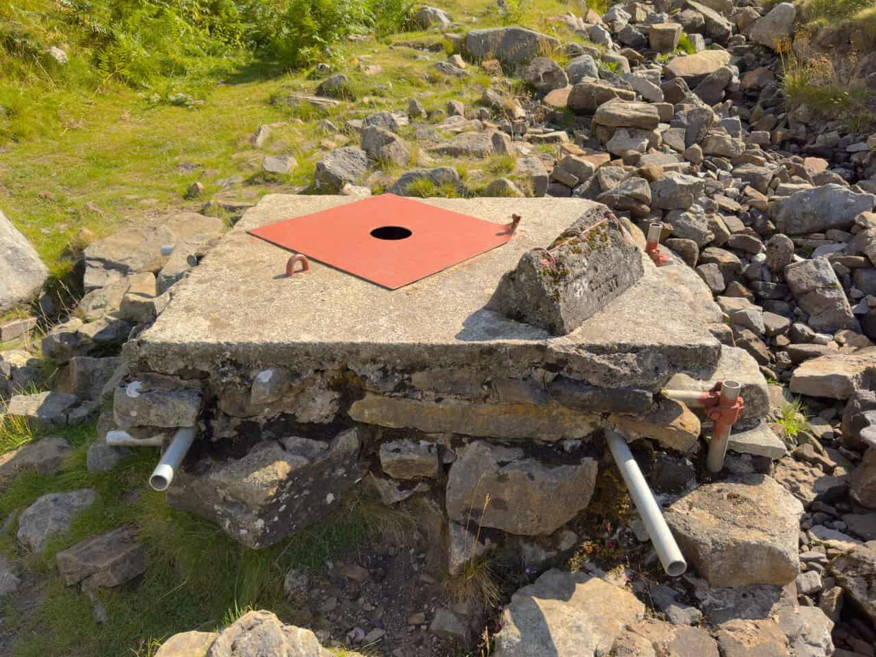 A close view of the concrete cap and red metal lid sealing the shaft at Providence Pot on the Great Whernside walk.