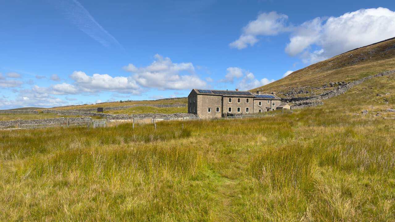The youth hostel at Hag Dyke standing alone on the flank of the mountain, seen across rough moorland grass.