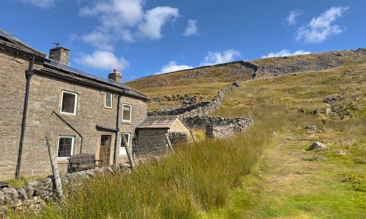 The stone buildings at Hag Dyke, with a dry stone wall climbing the rocky hillside behind.