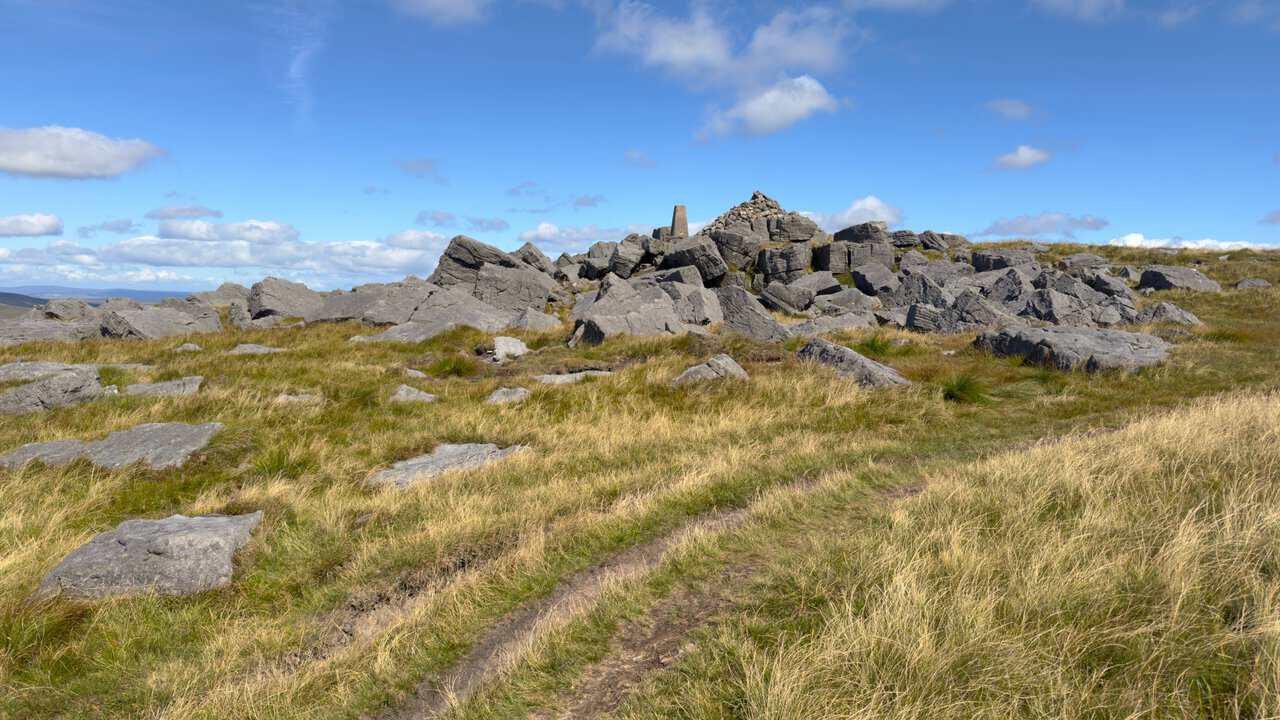 The triangulation pillar and summit cairn appearing above a broken sea of gritstone blocks.