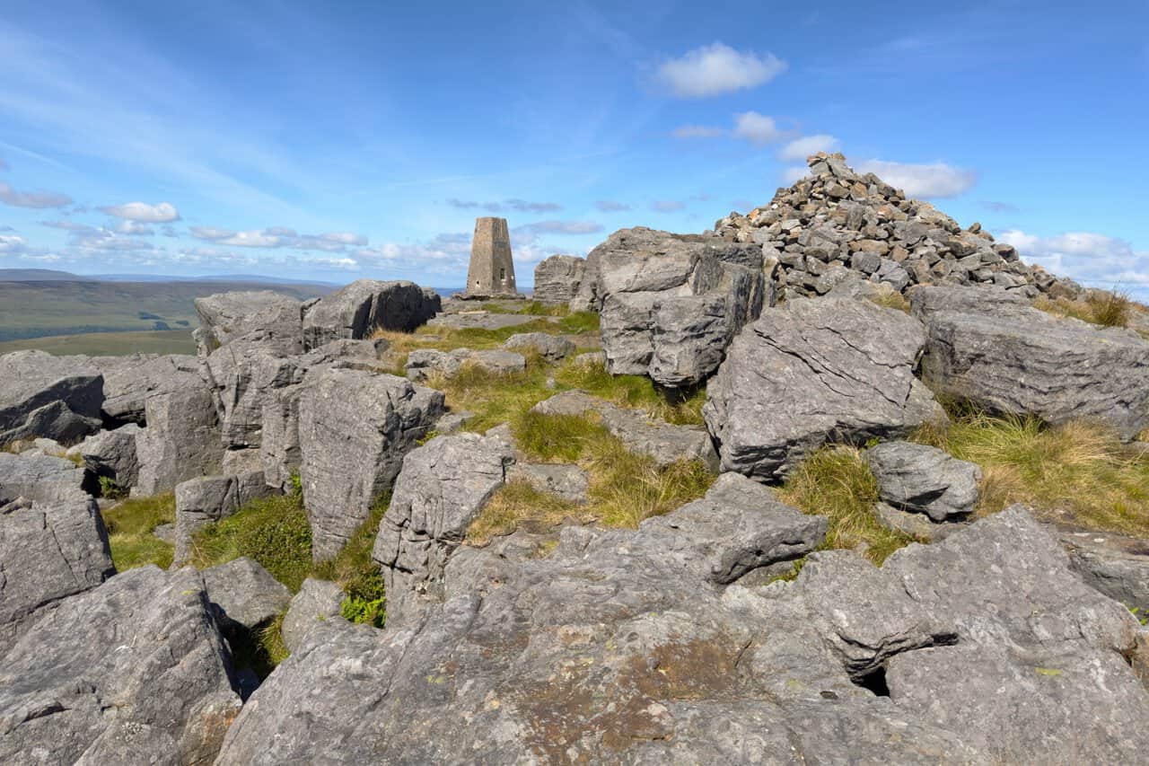 A closer view of the triangulation pillar beside the huge summit cairn, surrounded by tilted slabs of gritstone.