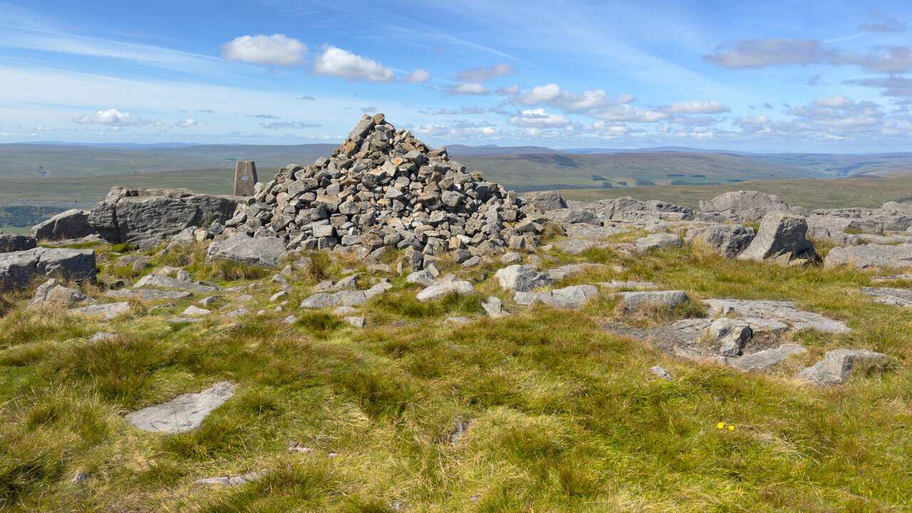 The huge summit cairn built up from loose stones, with the triangulation pillar standing behind it.
