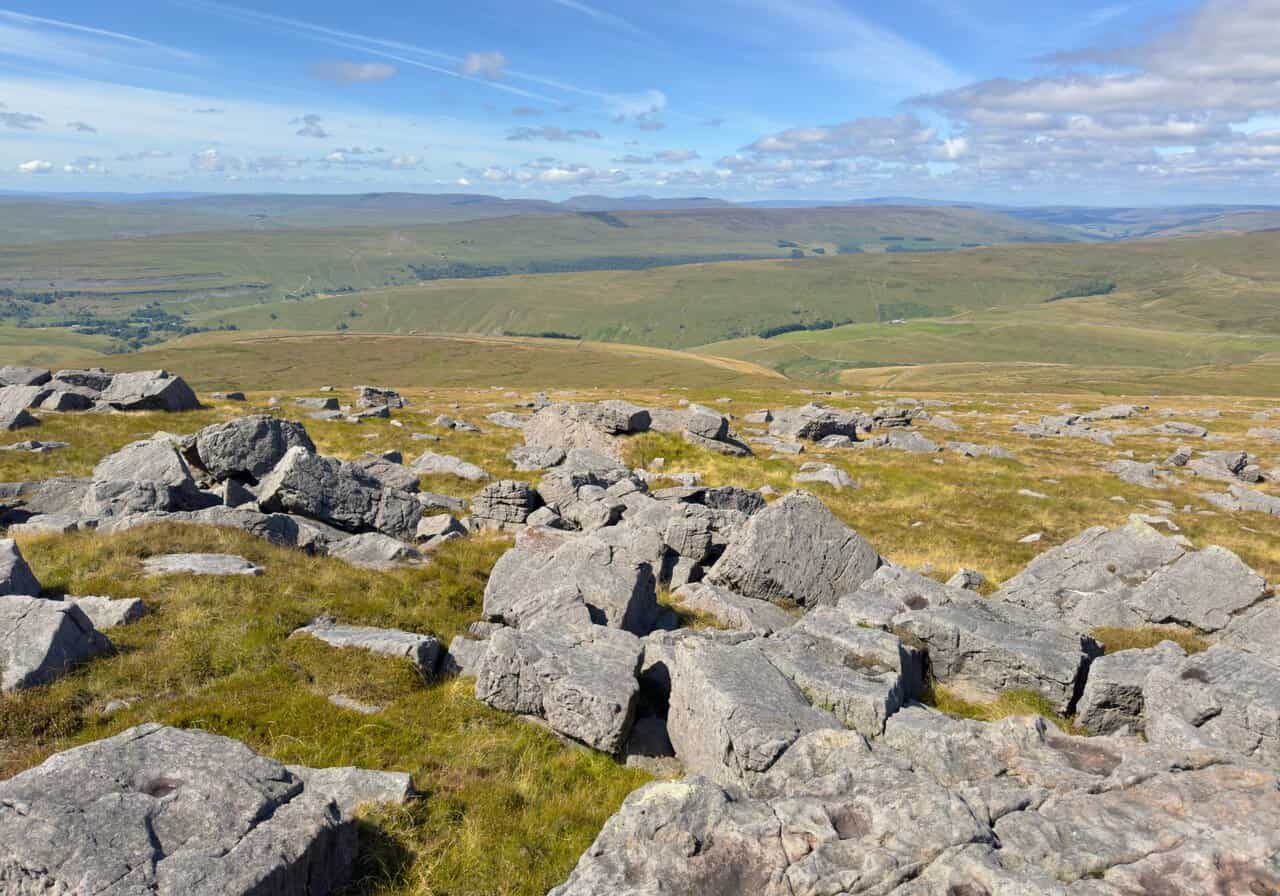 Scattered gritstone boulders along the ridge on the Great Whernside walk, with wide views west across the dales.