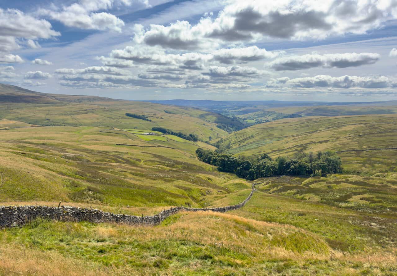 Looking down the length of Wharfedale from the head of the valley, with a dry stone wall running towards a wooded gill.