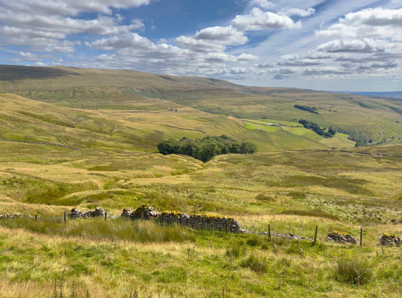 A ruined wall and old field boundaries on the open fell, with views east towards the higher moors.