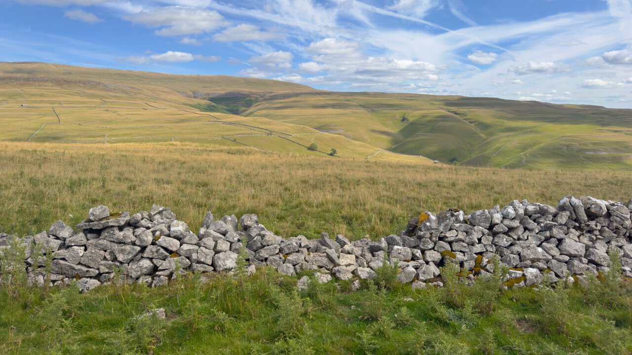 Light and shadow moving across the flanks of Great Whernside, with a ruined wall running along the fellside.