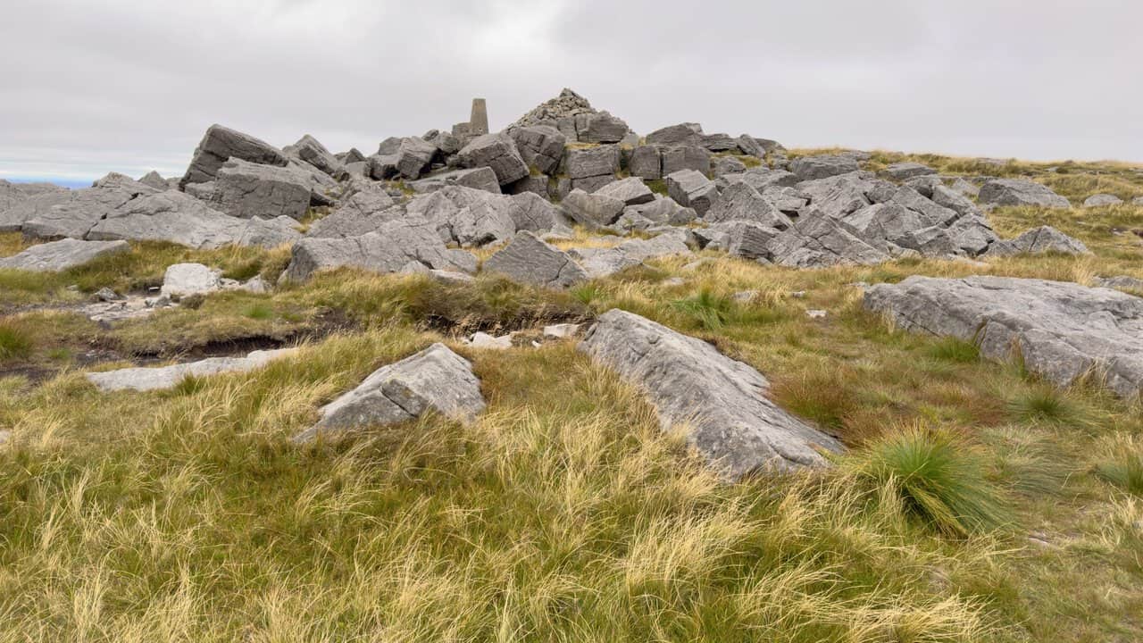 The summit of Great Whernside, with its triangulation pillar and cairn rising above a field of boulders on the highest point of both Great Whernside walks.