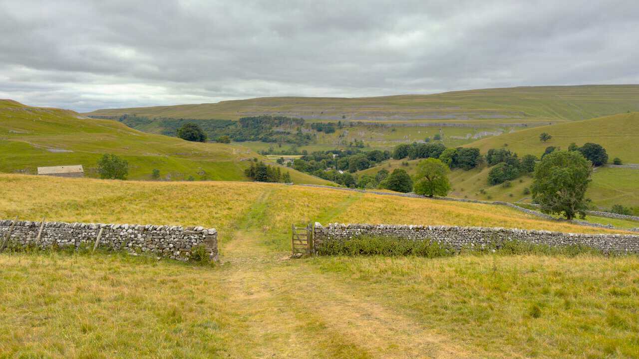 A gate in a dry stone wall framing the view down over Kettlewell and the Wharfedale valley.