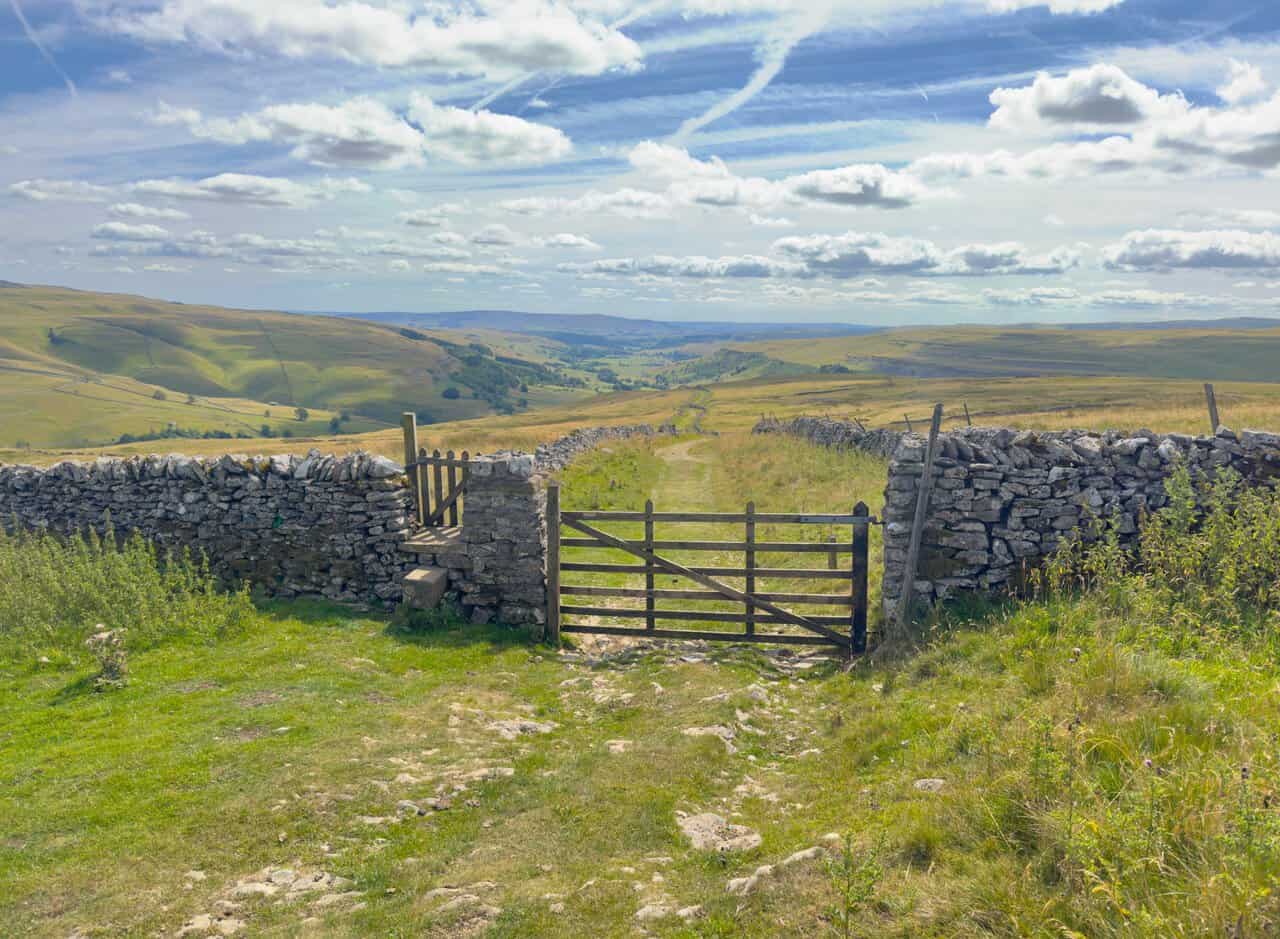 A wooden gate and stone stile on Top Mere Road, with the track running downhill towards Kettlewell.