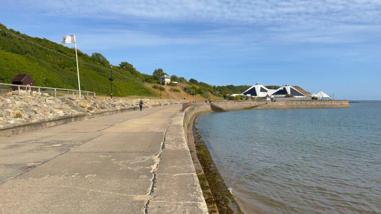 The promenade at North Bay curves along the sea wall, with the three white pyramids of Sea Life Scarborough visible in the distance and the tide up against the wall.