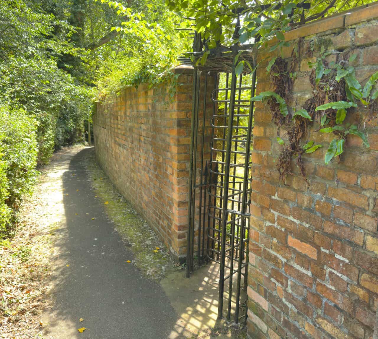 A wrought-iron rotating gate set into the brick wall of Manor Road Cemetery, with ferns growing from the brickwork above.