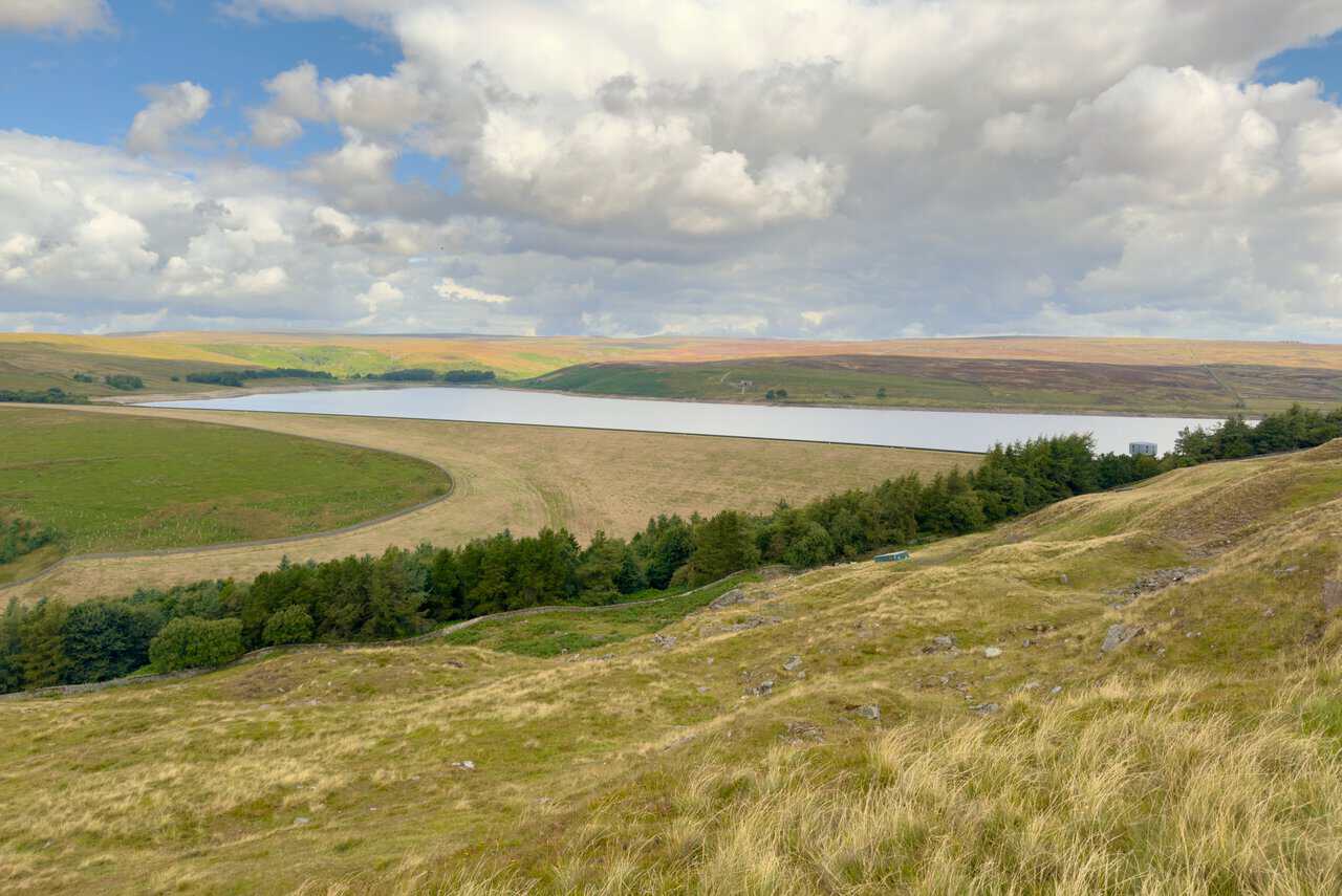 The full length of Grimwith Reservoir at the start of the Trollers Gill walk, with cloud shadows moving across the surrounding fells.