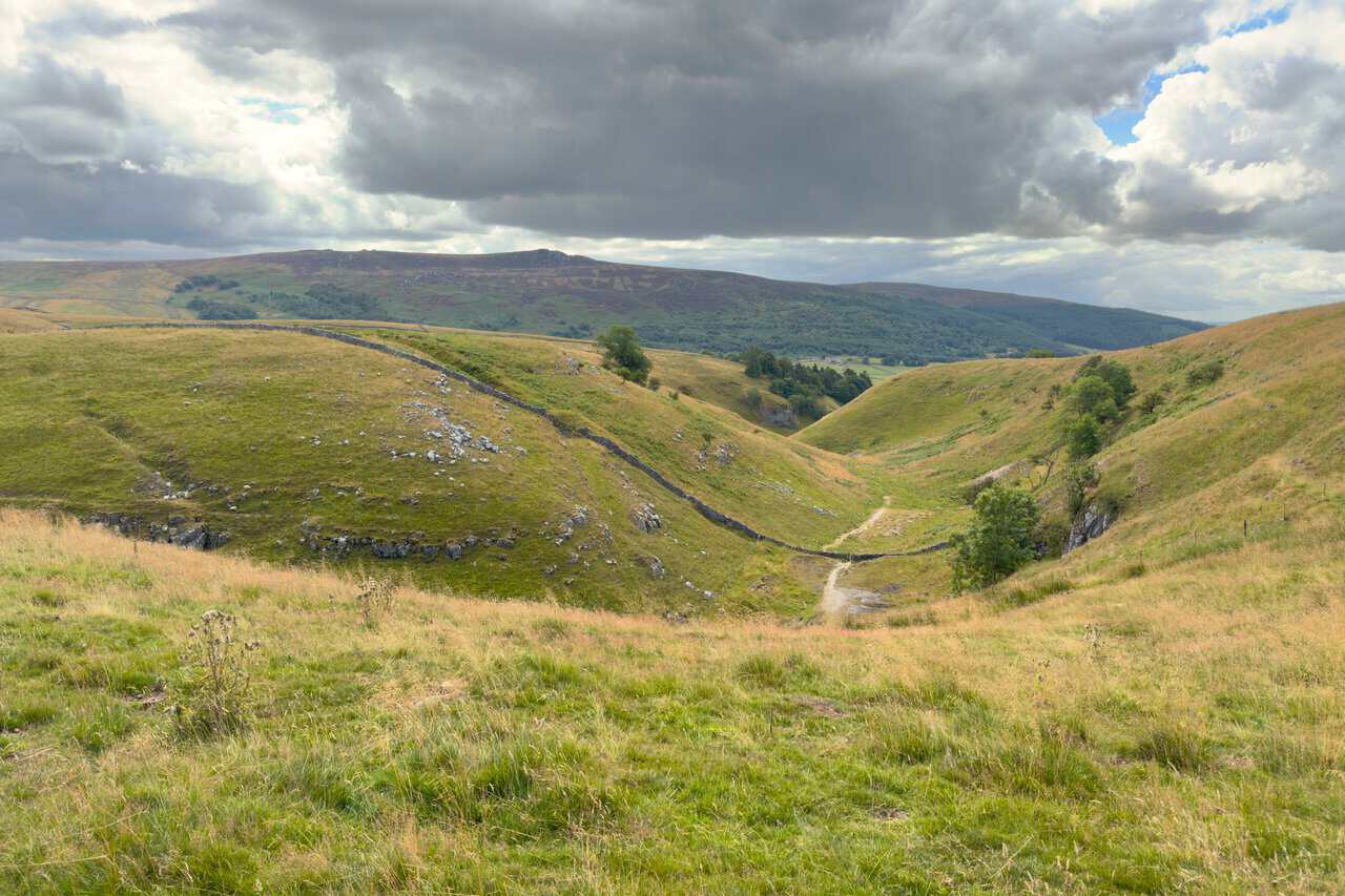 A shallow valley with a path running down through it, offering the wet weather alternative on the Trollers Gill walk.