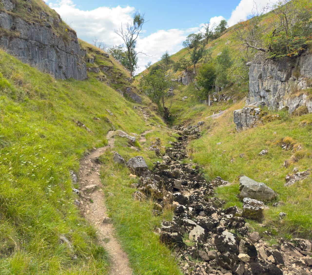 Grey limestone cliffs rising above a rough, stony channel as the valley narrows.