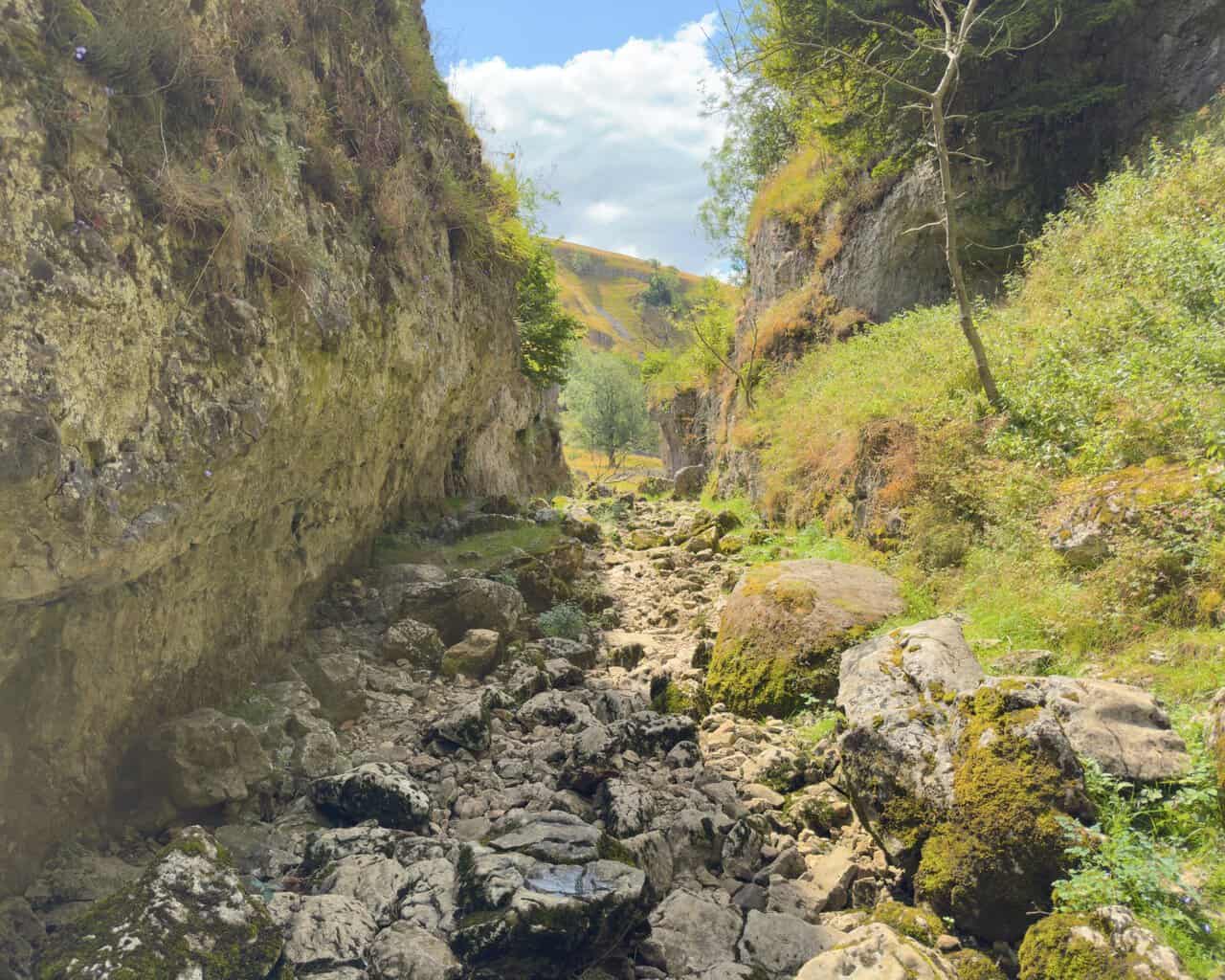 The final stretch of the ravine, with grey walls on the left and boulders scattered across the dry bed.