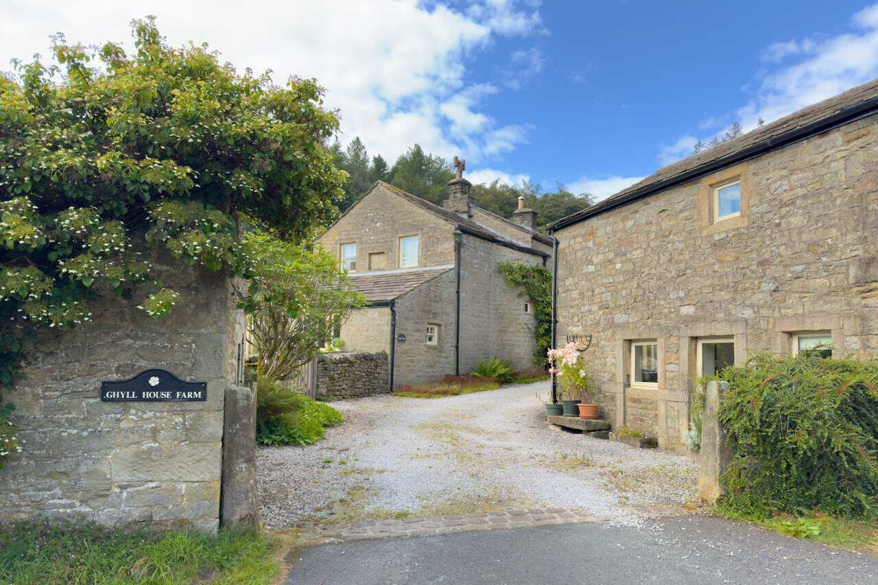 The stone buildings and gravel yard of Ghyll House Farm, with a name plate set into the wall.