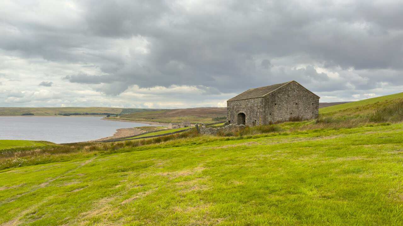 High Shaws Lathe, a stone barn with an arched doorway, standing above the shoreline on the Trollers Gill walk.