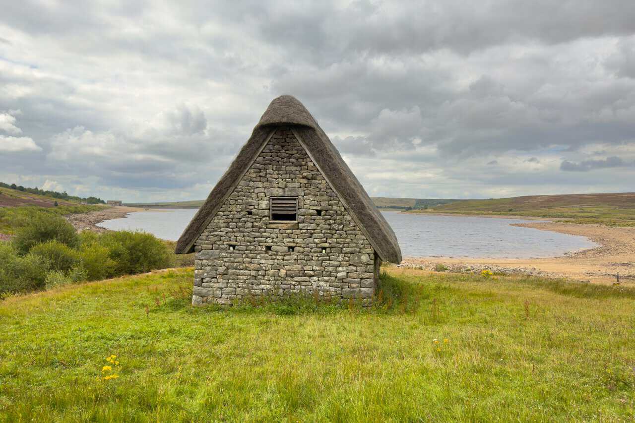 Grimwith High Laithe, a stone barn with a steep heather-thatched roof, beside the reservoir.