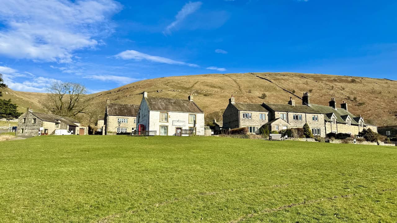 A white building with a red telephone box and a row of stone cottages beside the village green in Buckden.