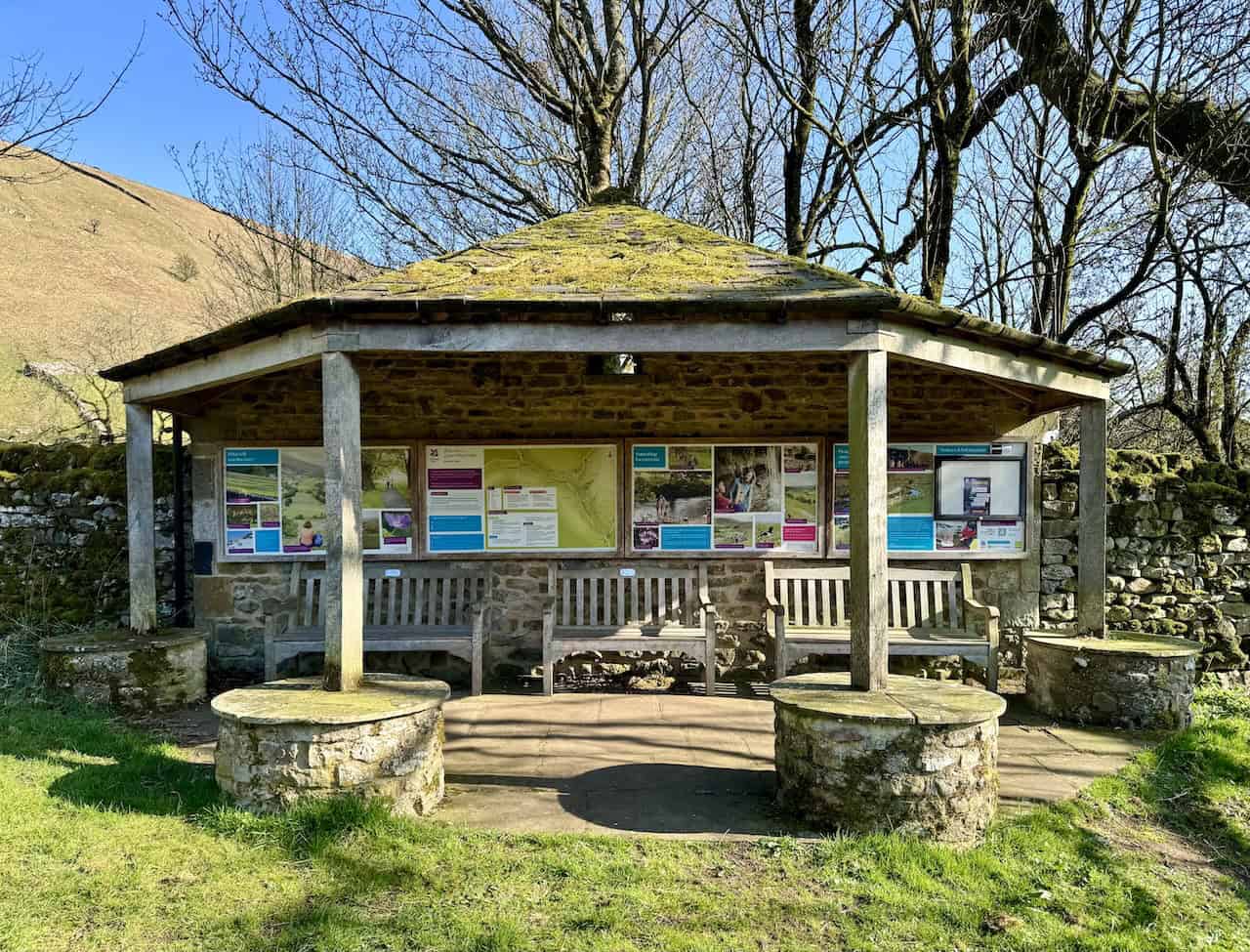 A stone shelter with a mossy roof, benches and information boards in Buckden, halfway round the Wharfedale 3 Peaks.