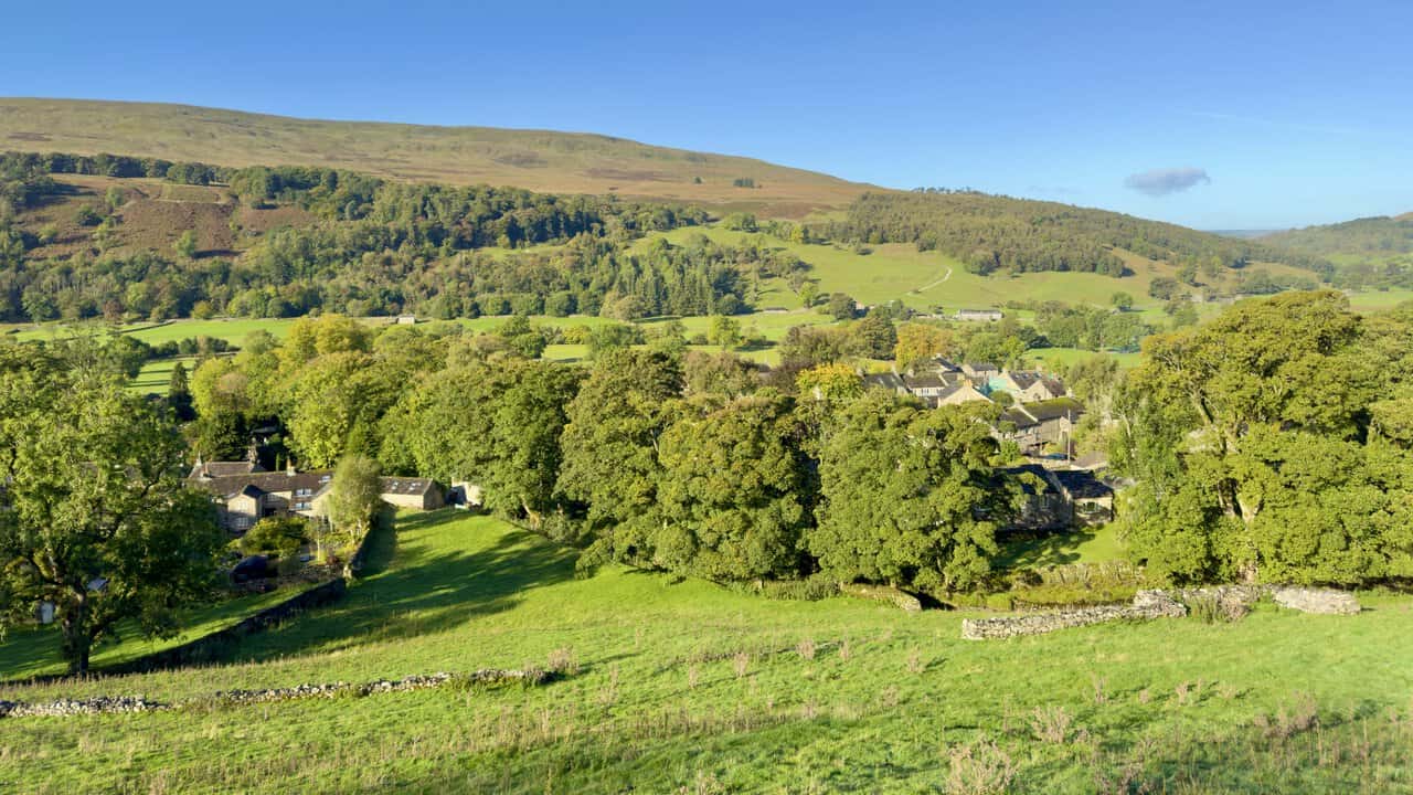 Buckden village among trees and fields in Upper Wharfedale, seen from the lower slopes of Buckden Pike.