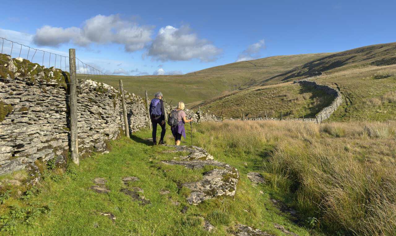 Two walkers following a dry-stone wall towards Buckden Lead Mine on the slopes of Buckden Pike.