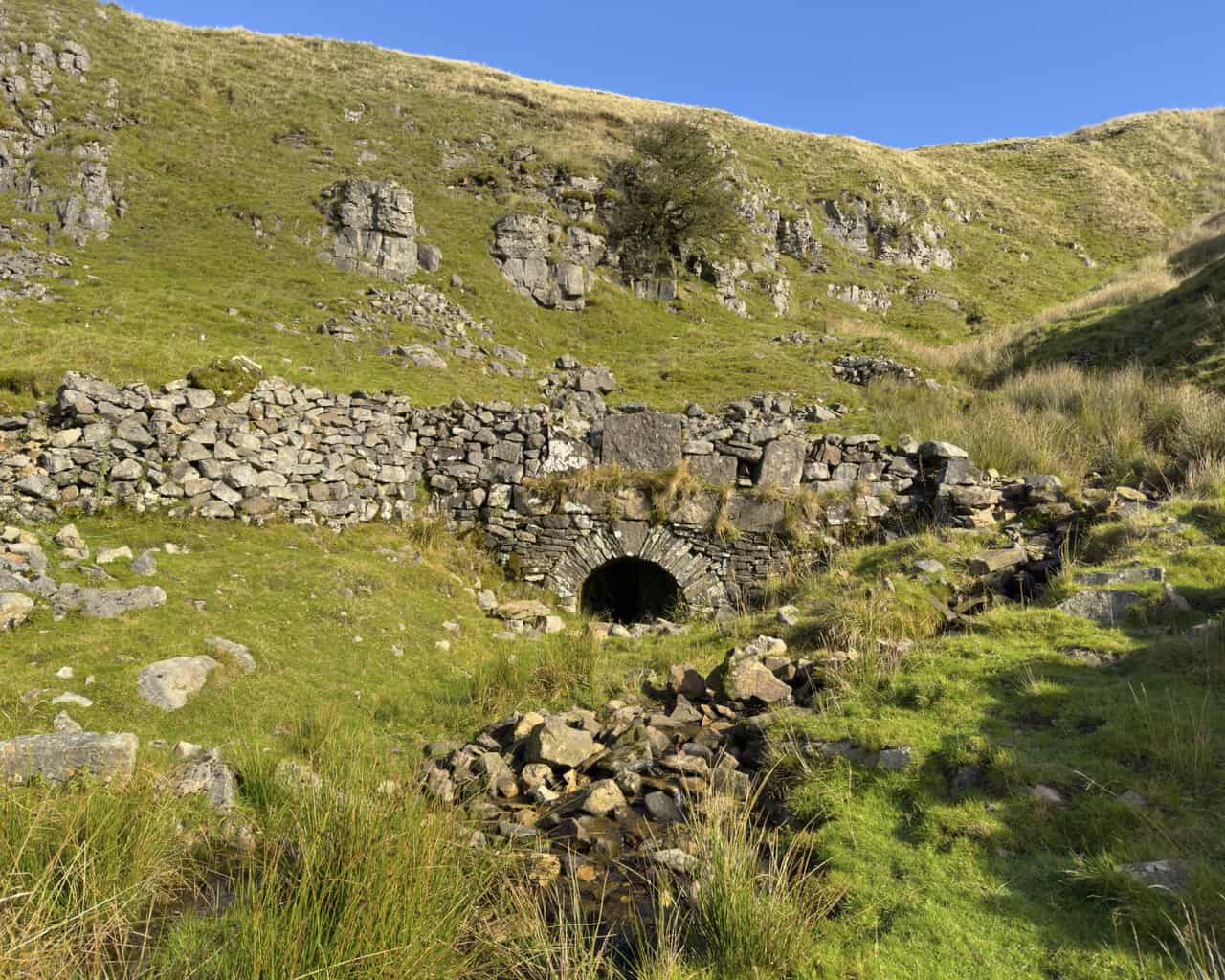The stone-arched adit entrance at Buckden Lead Mine, with water trickling out beneath it.