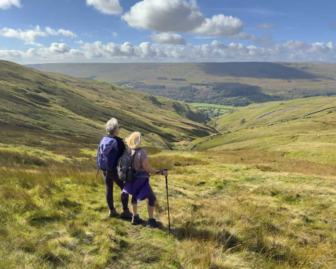 Two walkers pausing to admire the view down the valley during the steep climb to Buckden Pike.