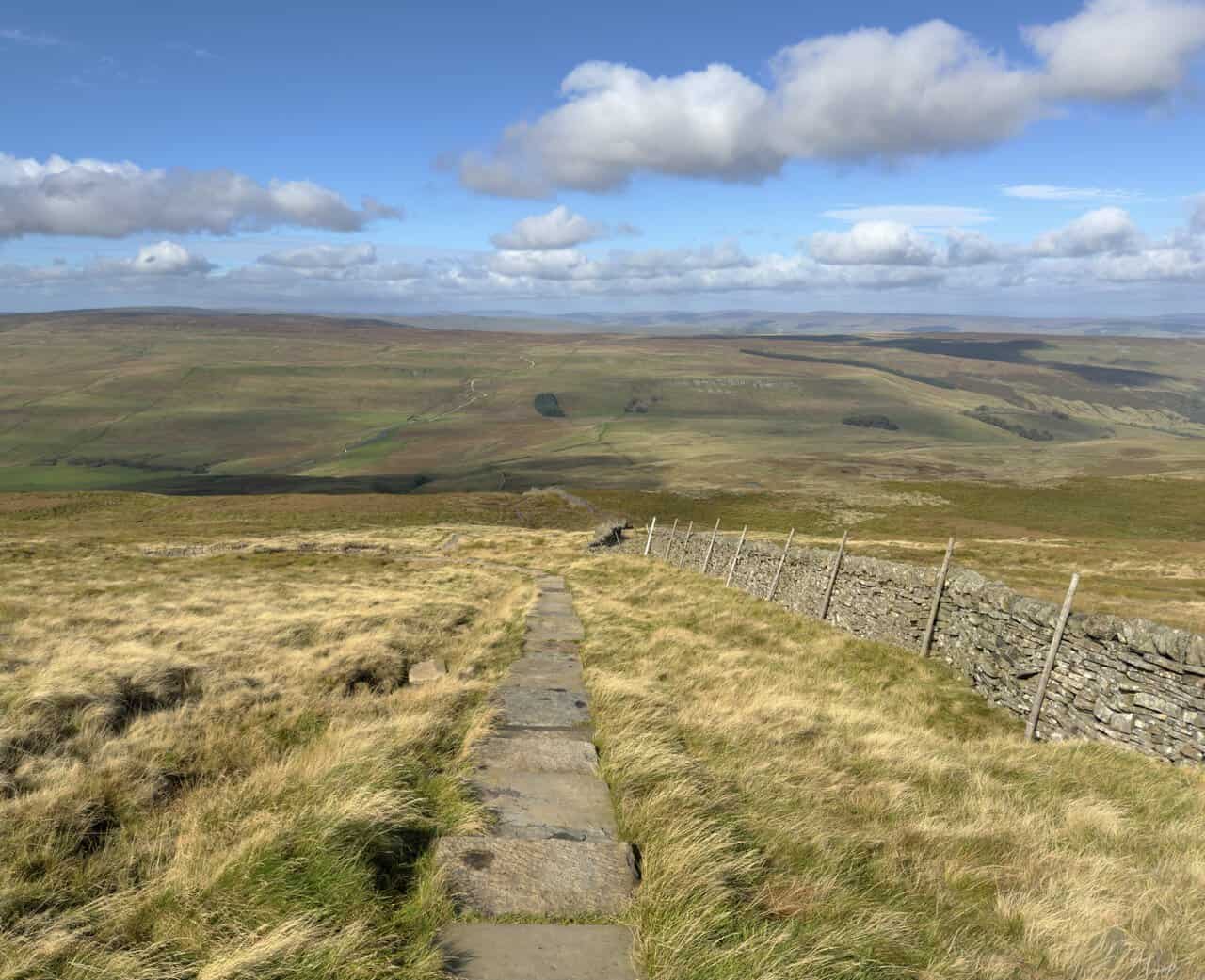 A line of stone flags beside a dry-stone wall at the start of the descent from Buckden Pike.