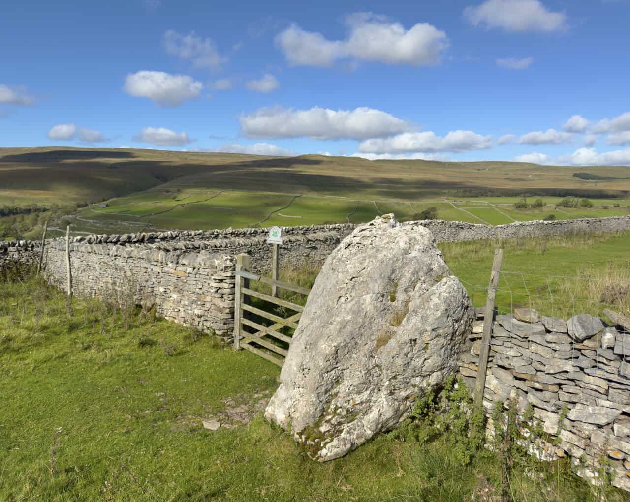 A large limestone boulder beside a gate and dry-stone wall at Buckden Rake.