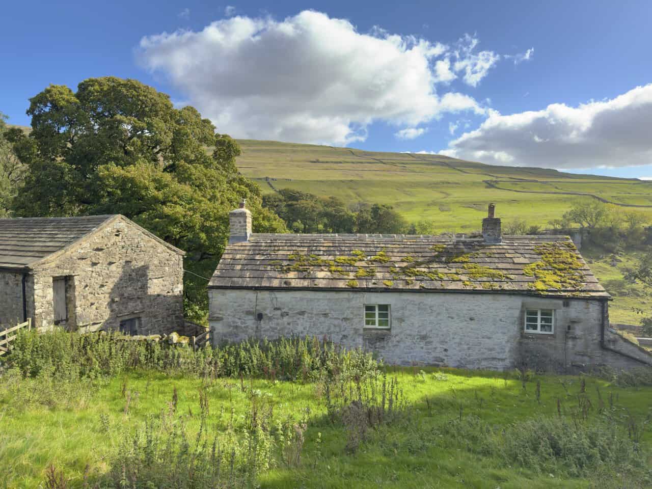 Stone farm buildings at Cray, with the green slopes of Buckden Pike rising behind.