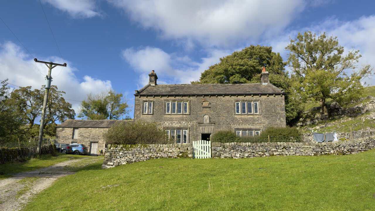 The stone front of Scar House, with its mullioned windows and datestones above the door.