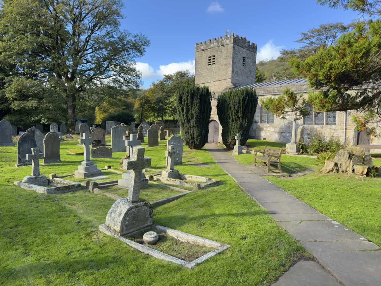 A flagged path between yew trees leading to the entrance of St Michael and All Angels Church, Hubberholme.