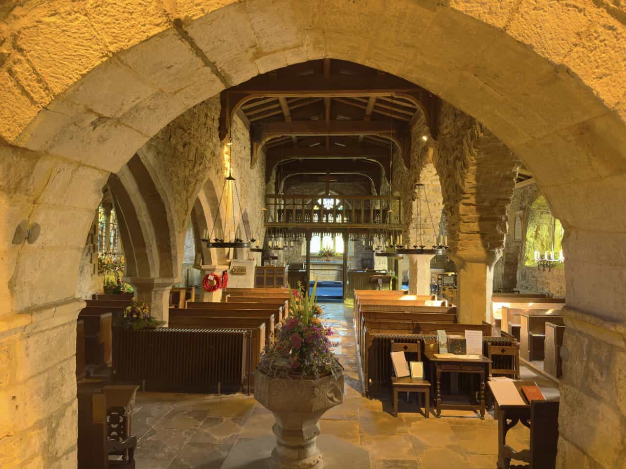 The font and wooden rood loft seen through a stone arch inside St Michael and All Angels Church.